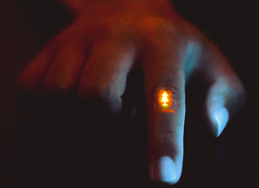 曲げた指関節上でスタンフォード大学のロゴを映し出す、皮膚貼付型の発光フィルム。